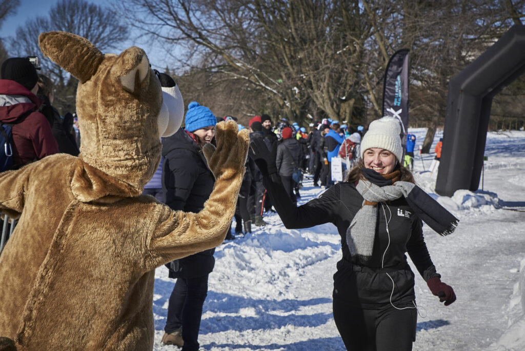 Une coureuse souriante fait un « high-five » à Cachou, la mascotte de la Fondation CHU Sainte-Justine.