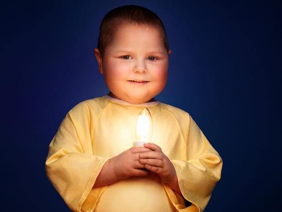 Rosalie, 3, a young Sainte-Justine patient who has lost her hair to chemotherapy, holds a lit, flame-shaped light bulb in her hands. She is wearing a blue hospital smock.