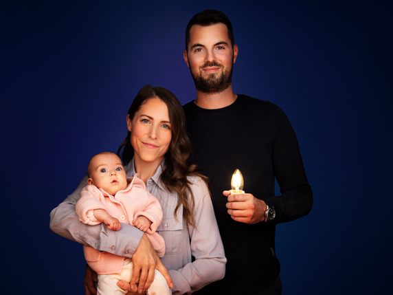 Annie, holding a six-month-old Béatrice in her arms, stands beside Nicholas, who has a glowing light bulb in his hands.