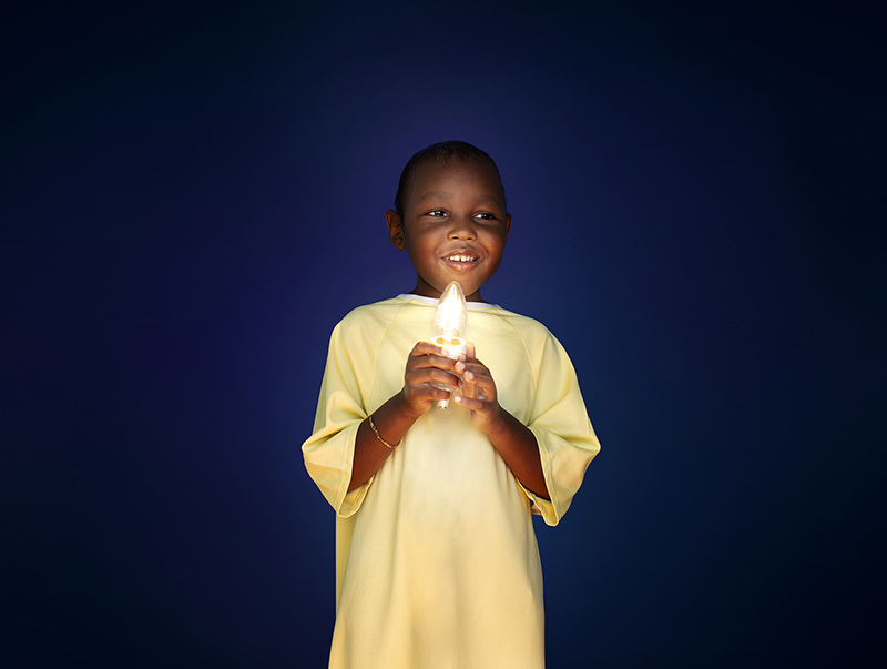Eli-Noah, 5 ans, porte une jaquette jaune et tient une ampoule allumée entre ses mains.