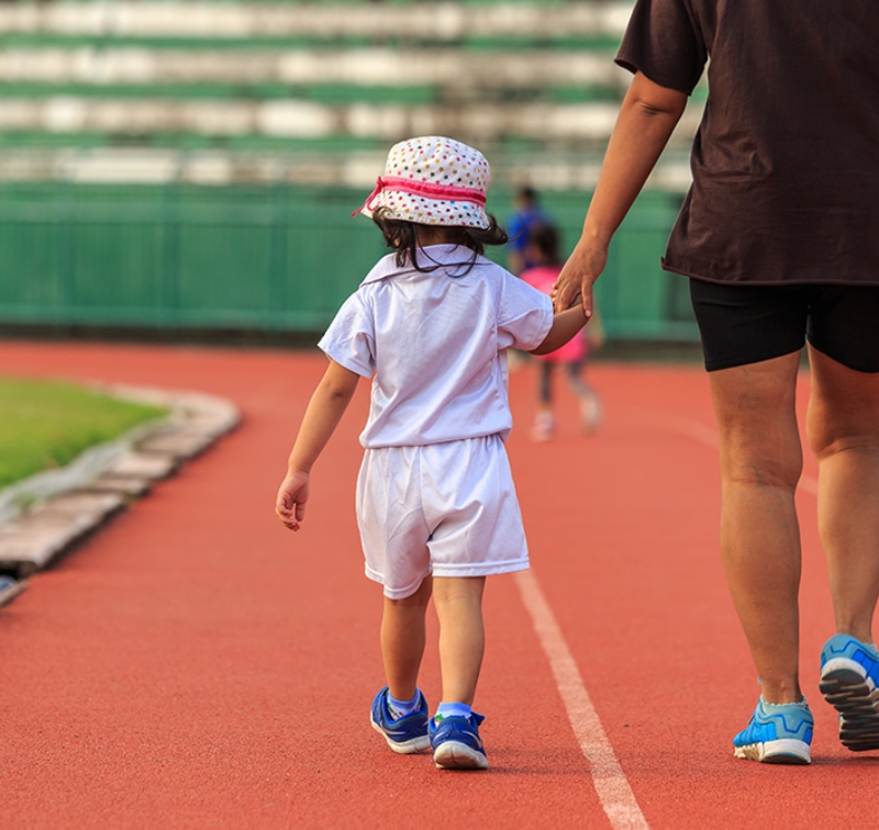 Fille tenant la main à un parent qui marche sur une piste de course