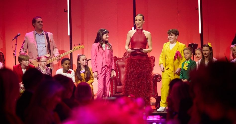 Karine Vanasse parle au micro sur une estrade, entour&eacute;e d&rsquo;enfants. 
