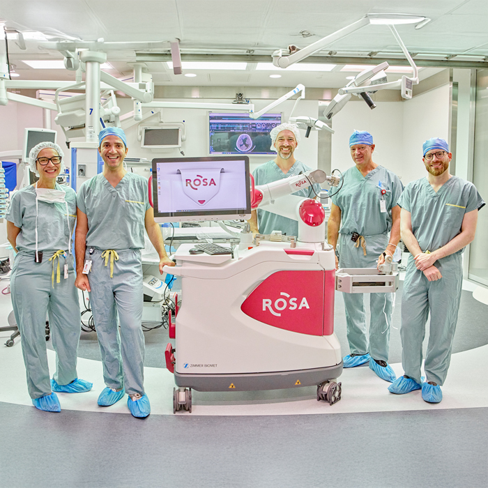 La Dre Inge Meijer et les Drs Aris Hadjinicolaou,  Philippe Major, Dominic Venne et Alexander Weil dans une salle d&rsquo;op&eacute;ration, autour du robot neurochirurgical ROSA. 