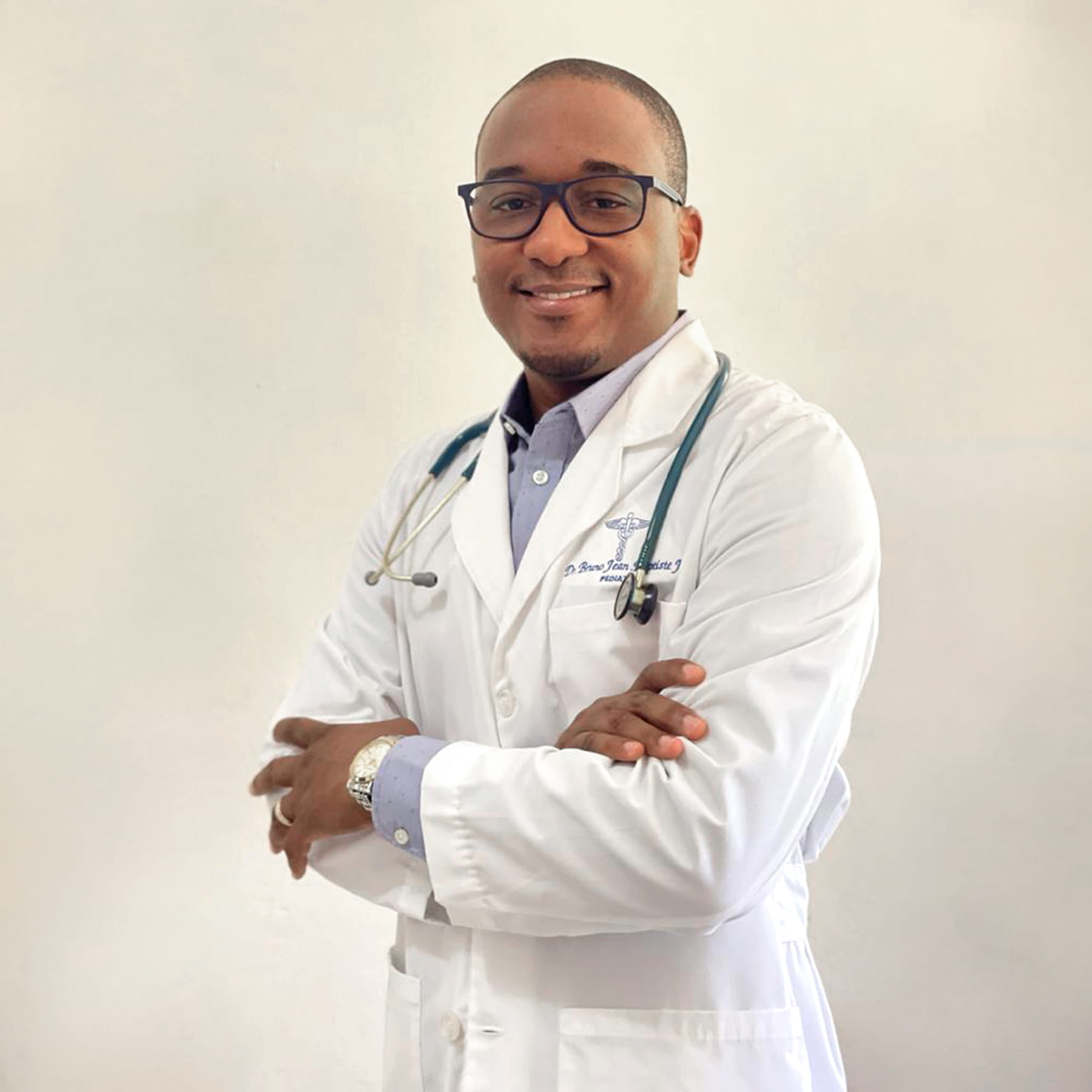 Un médecin en sarrau blanc, stéthoscope au cou, sourit en regardant la caméra.  