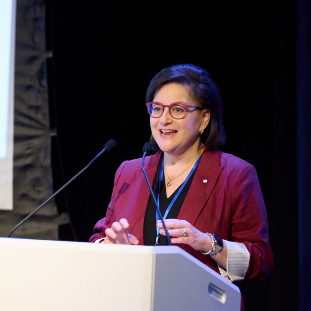 A woman speaks at a lectern, smiling.