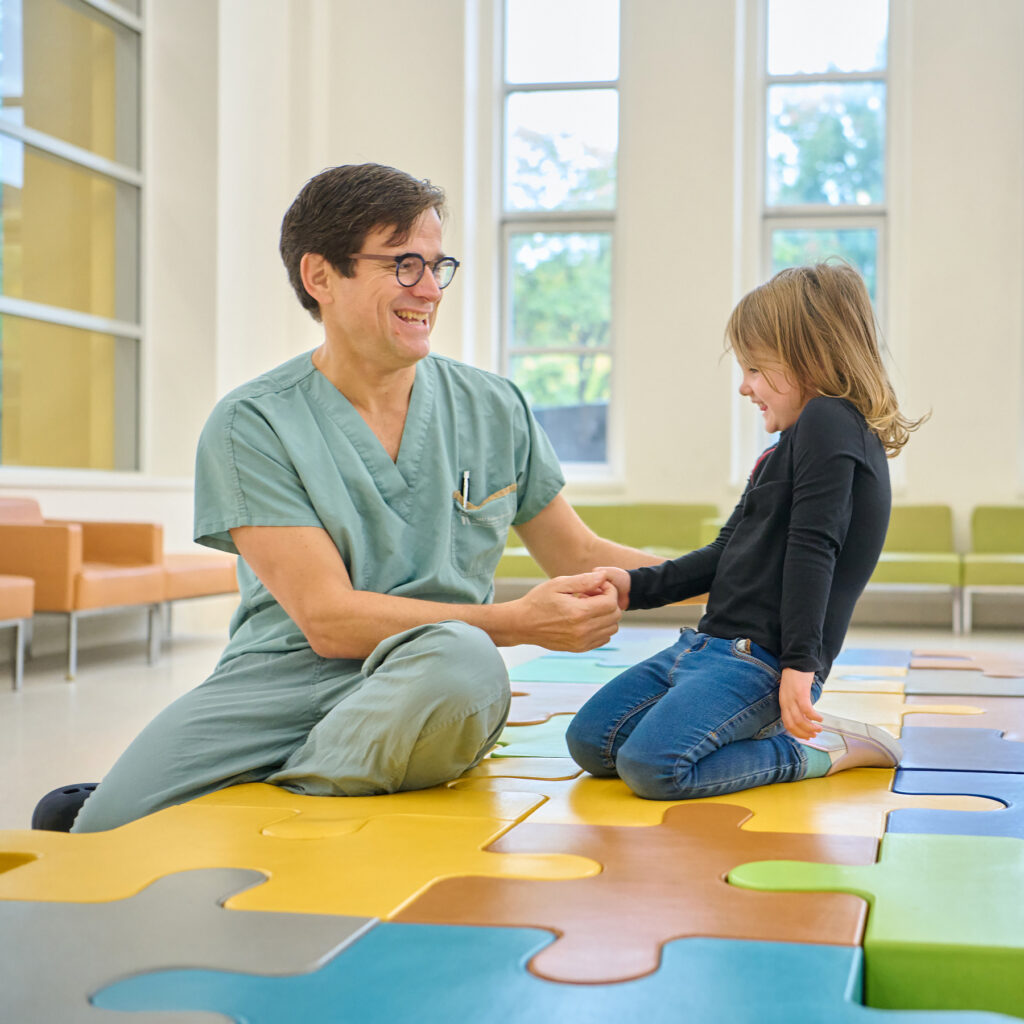 A little girl laughs with a man in medical attire.
