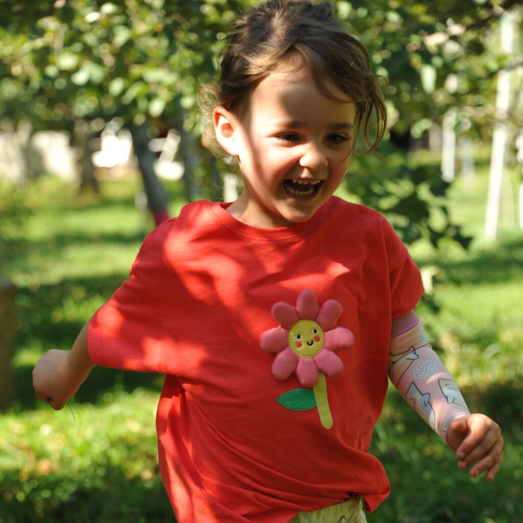 A little girl runs outside, laughing. 
