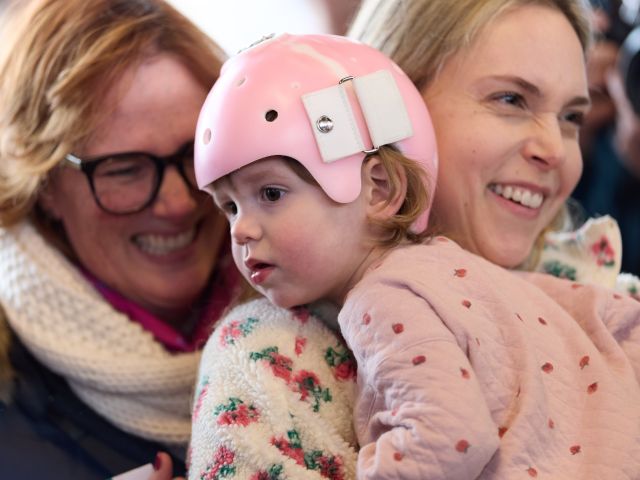 A little girl wearing a pink helmet is held in a woman’s arms.