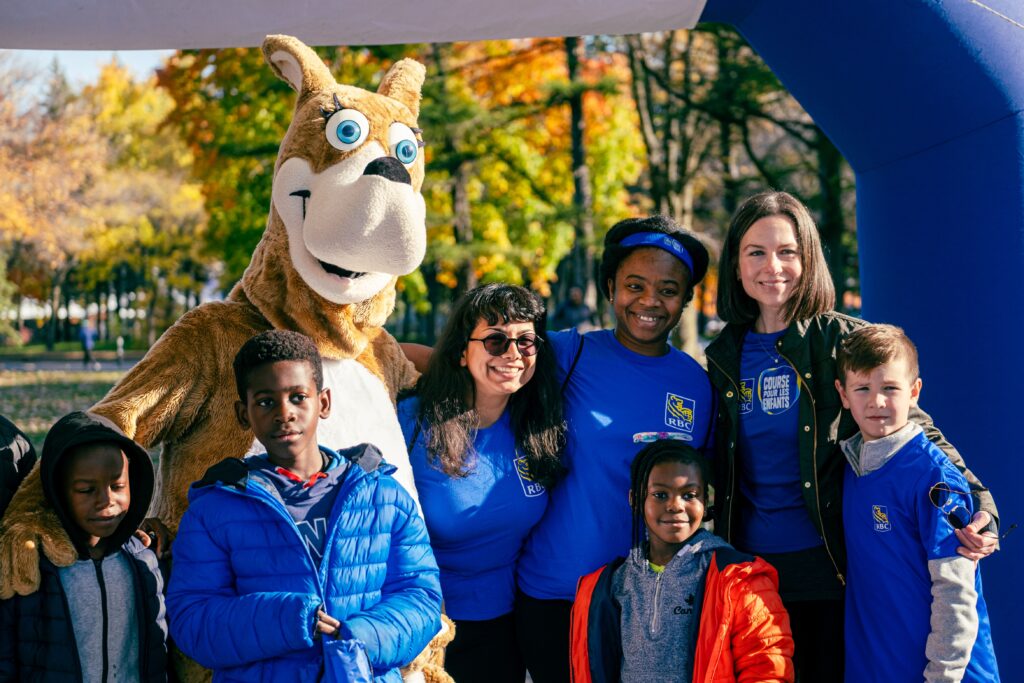 RBC employees and their families, posing outside with Nadine Renaud Tinker, president of RBC Quebec, and Cachou, Sainte-Justine’s mascot. 